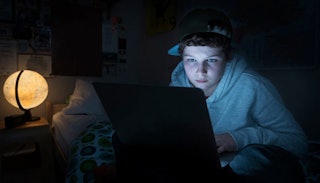 A boy sitting alone and using his laptop in the dark late at night