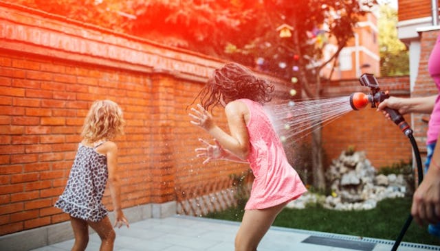 Two little girls having fun during the summer heat with a water sprinkler.
