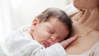 A rainbow baby in a white shirt laying on mother's chest