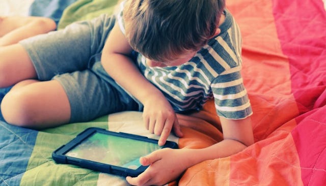 A trans child playing on a tablet on a LGBTQ inspired bedding