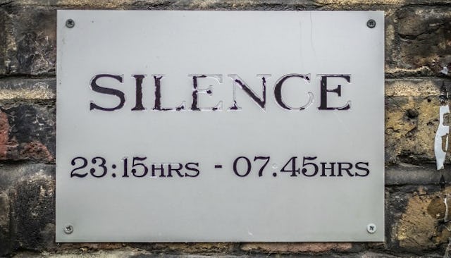 A metal sign on a brick wall warning about silence hours.