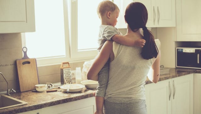 A woman who used to judge SAHMs until she became one standing in a kitchen and holding her baby whil...
