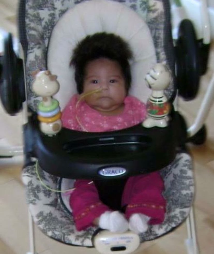 A baby placed in a baby highchair with medical tubes attached to its nose