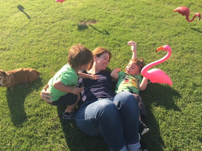 A smiling mother with her two kids lying on grass with three flamingo sculptures