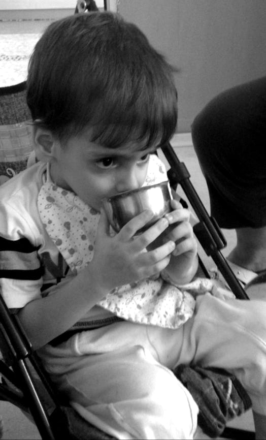 A boy drinking from a metal cup in a stroller