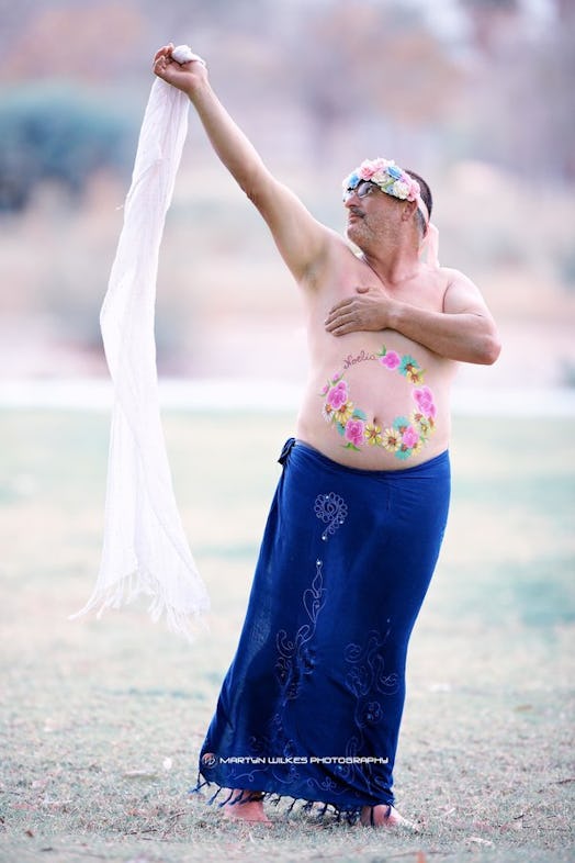 A dad covering his breasts and holding his veil into the wind while posing for a maternity photo 