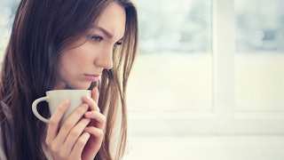 A woman holding a cup under her chin while looking sad