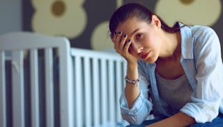 Woman Holding Hear Head And Sitting In Front Of A Baby Crib As She Feels Like Being Trapped In 'Baby...