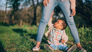 A mom in light blue denim jeans and loafers standing above a child in a light blue and orange checke...