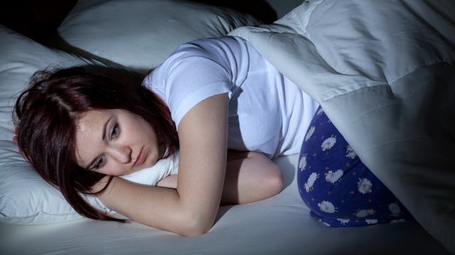 A woman with Premenstrual Dysphoric Disorder lying awake and uncovered in bed