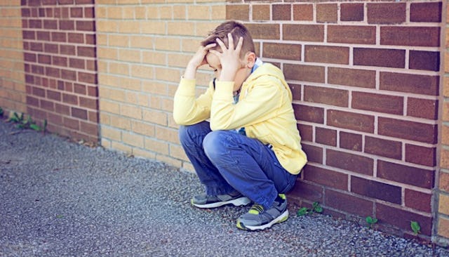 A sad boy sitting on the floor leaning on the wall holding his head because he didn't get a prize
