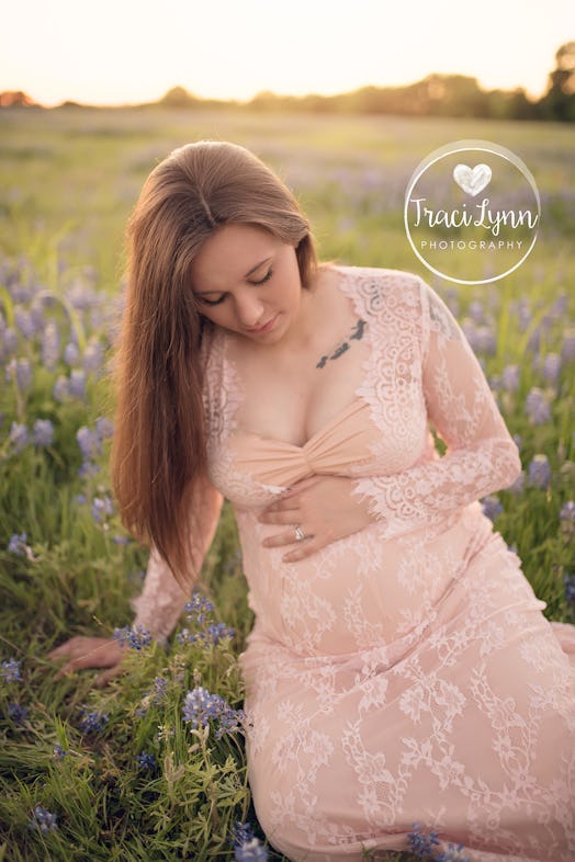 A pregnant woman sitting down in the grass, holding her belly and posing for a picture.