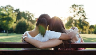 Two reconciled girls sitting hugged on a bench