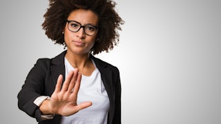 Curly-haired woman wearing glasses, signaling "stop" with her hand in terms of asking someone about ...