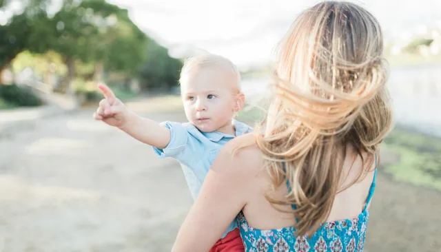 A mother in a blue dress holding her son who's pointing at something in the distance