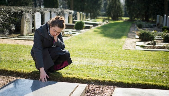 A woman sitting beside her mother's grave and looking at it 