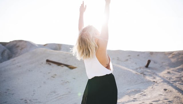A short-haired blonde woman in a white top and black trousers with her hands up enjoying her life at...