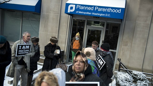 A group of people protesting with 'I am pro life' poster in front of a Planet Parenthood office