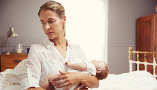 A woman in white holding her newborn daughter looking to the side while experiencing anxiety