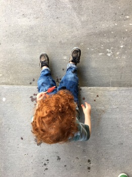 A red haired boy sitting on the stairs and eating ice-cream.