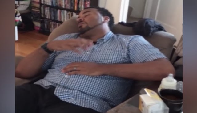 A dad in a blue shirt sleeping in an armchair while comforting an imaginary baby 