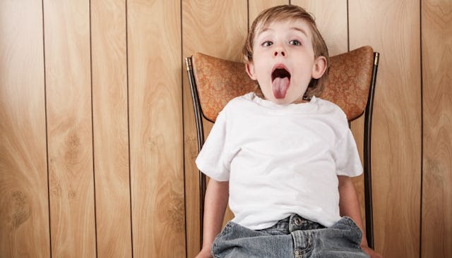 A kid on a chair having a time-out showing his tongue