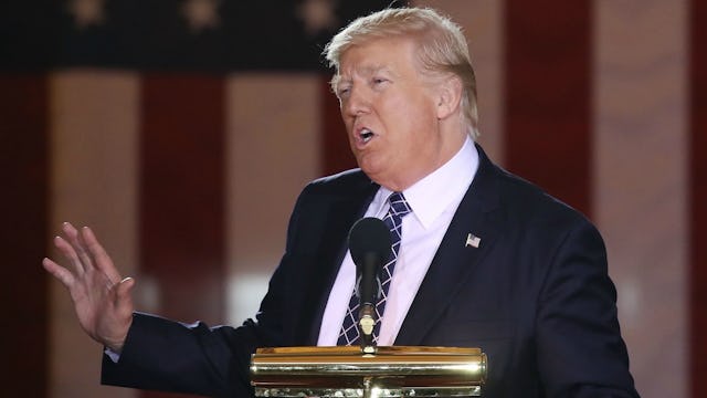 Politician Donald Trump wearing a black suit and white shirt talking at the stage with one of his ha...