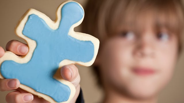 A kid with autism holding a blue-white cookie in the shape of a puzzle piece.