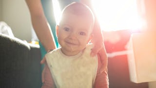 Baby being held by mother's hands and smiling with its head tilted to the side