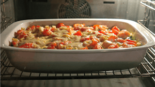A photo of casserole in a white container sitting in a turned on oven