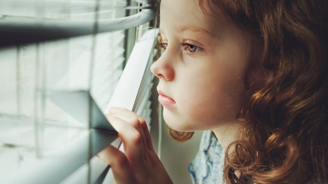 A little girl looking through the blinds at the window