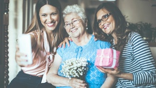 A young woman taking a selfie with her mother and grandmother on Mother's Day while smiling and posi...