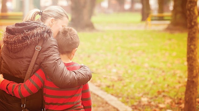 A mother who loves her kid more than her ex while holding and kissing him in a park during a sunny d...