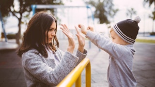 A mother in a grey sweater clapping both hands with the hands of her son in a grey shirt and a black...