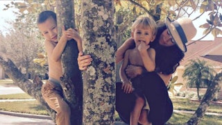 Amanda Elder holding her younger son while the older one is climbing the tree.
