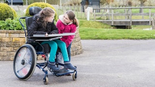 A child with special needs sitting in a wheelchair and talking to her friend in a park