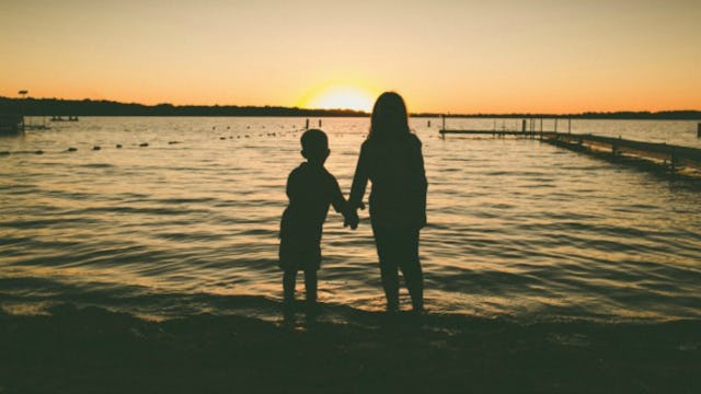A mother with a perfect beach body and a boy holding hands slightly darkened, watching the sunset wi...