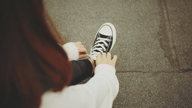 A mid-thirty woman tying her shoelaces on All Starts Converse sneakers
