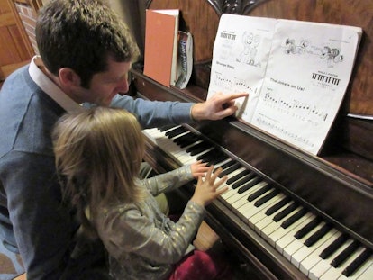 A dad teaching his daughter how to play the piano