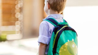 A little boy carrying a small backpack on his way to kindergarten