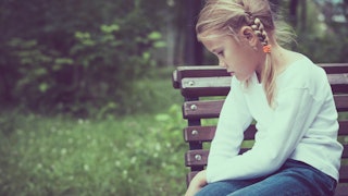 A blonde female child sitting in a park looking sad