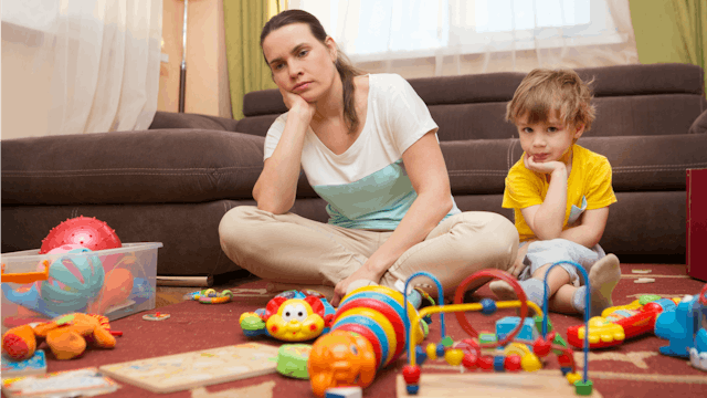 Young mom wearing a white t-shirt is bored while playing with her son on the floor on Mother's day