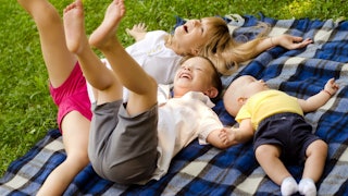A girl and two boys lying down on the blanket at the park and laughing.