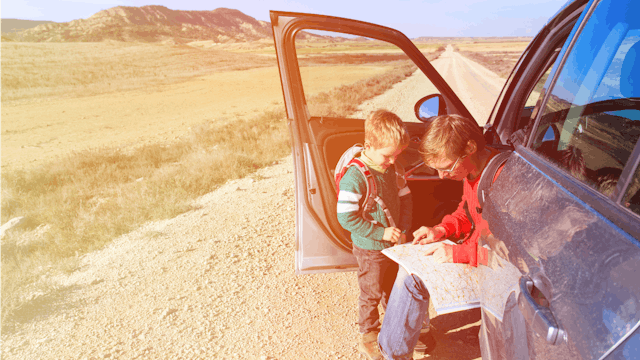 A father traveling with his son, sitting in an open car checking his map in the middle of the road