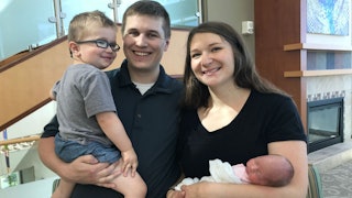 A mom holding a newborn and a dad holding a toddler while they're smiling and posing