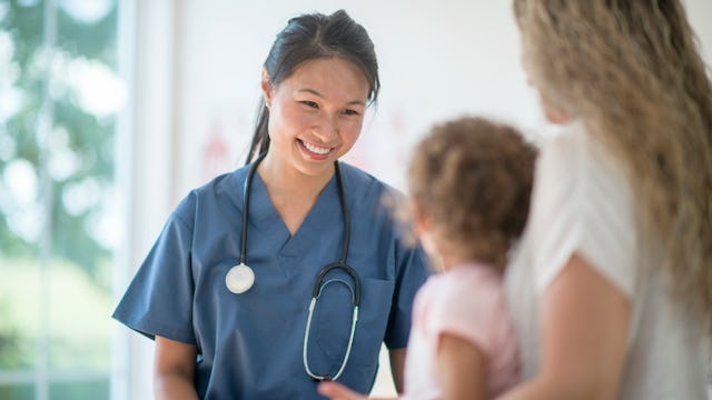 A nurse smiling at a girl who's standing next to her mom