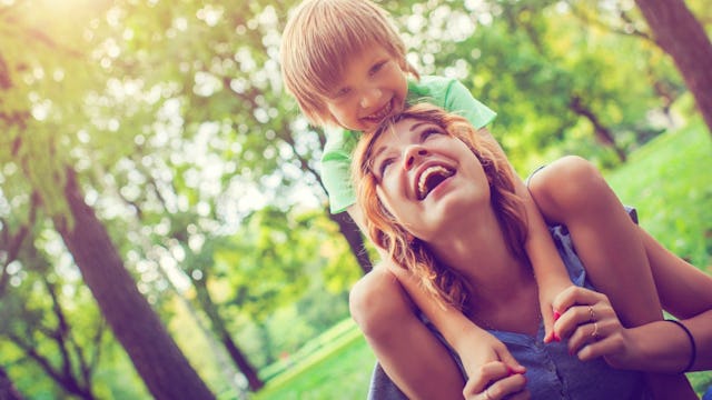 A happy parent holding a child on her shoulders in the park.