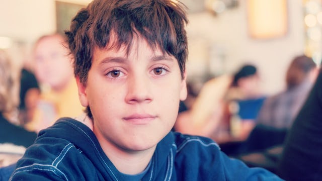 A brown-haired child with special needs, wearing a blue shirt while looking toward the camera 