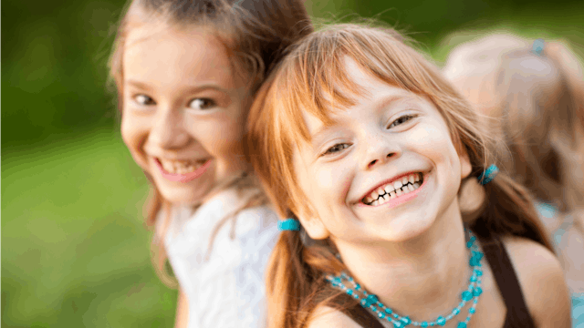 Two sisters smiling and posing together while playing outside