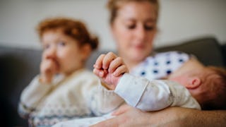 A mother holding her baby in her arms and her toddler sitting next to them and eating an apple